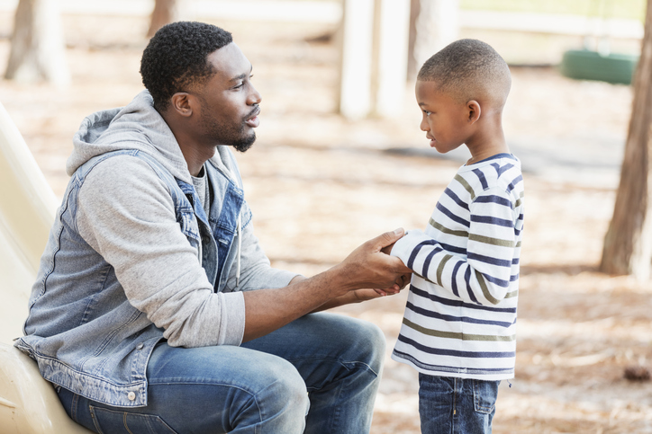 Father holding child's hand talking to him calmly